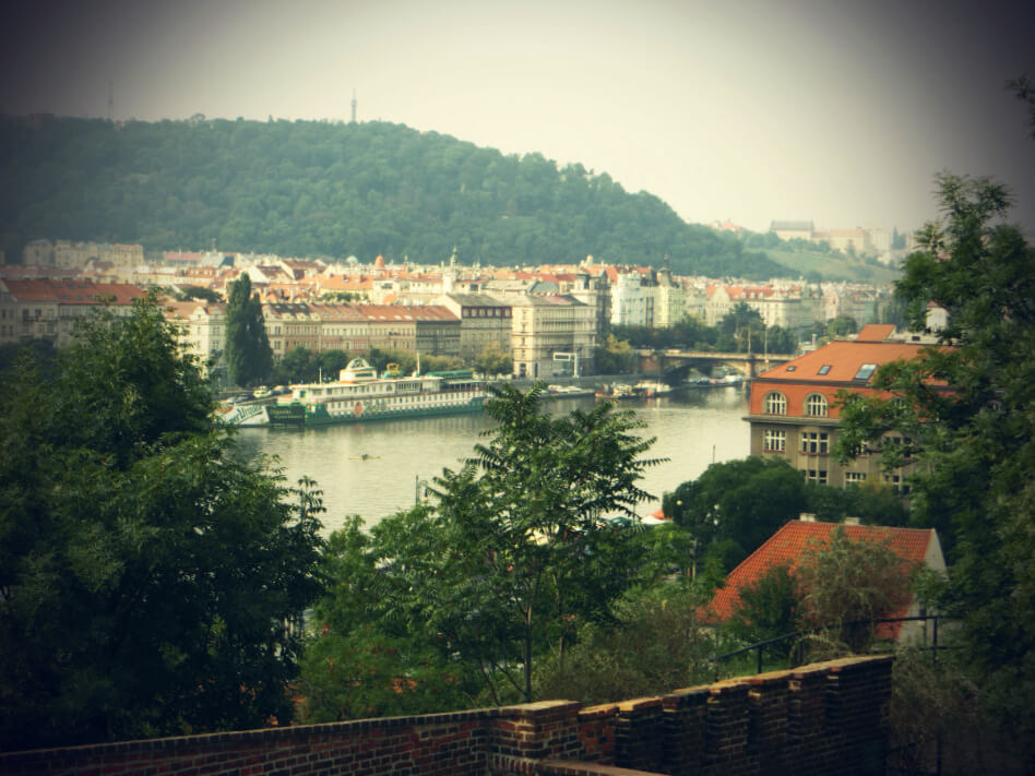 A photographic view of the Prague river and the buildings on the banks with many red clay tiled roof tops.